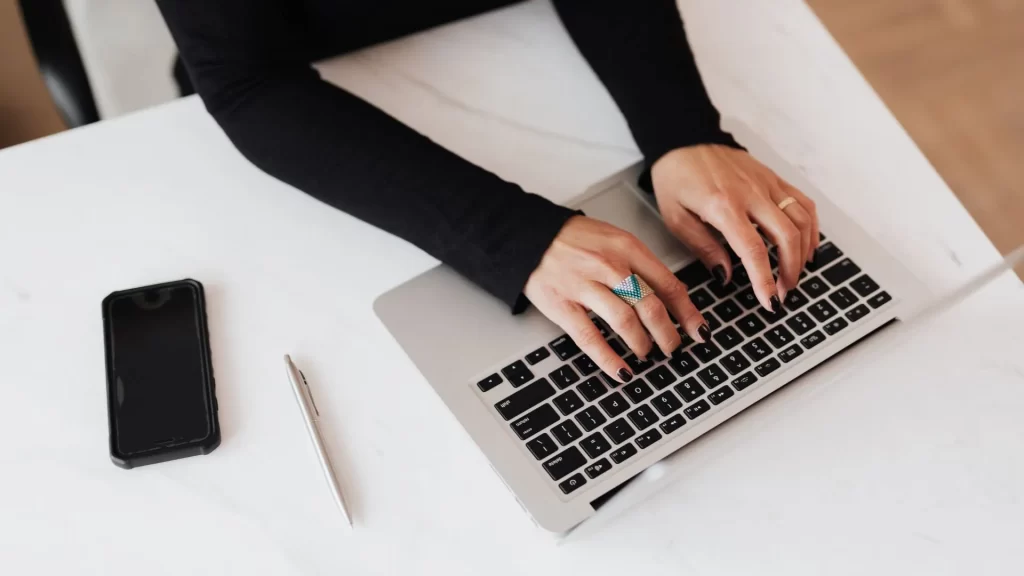 A woman’s hands decorated by rings are seen typing on a laptop’s keyboard keys. 