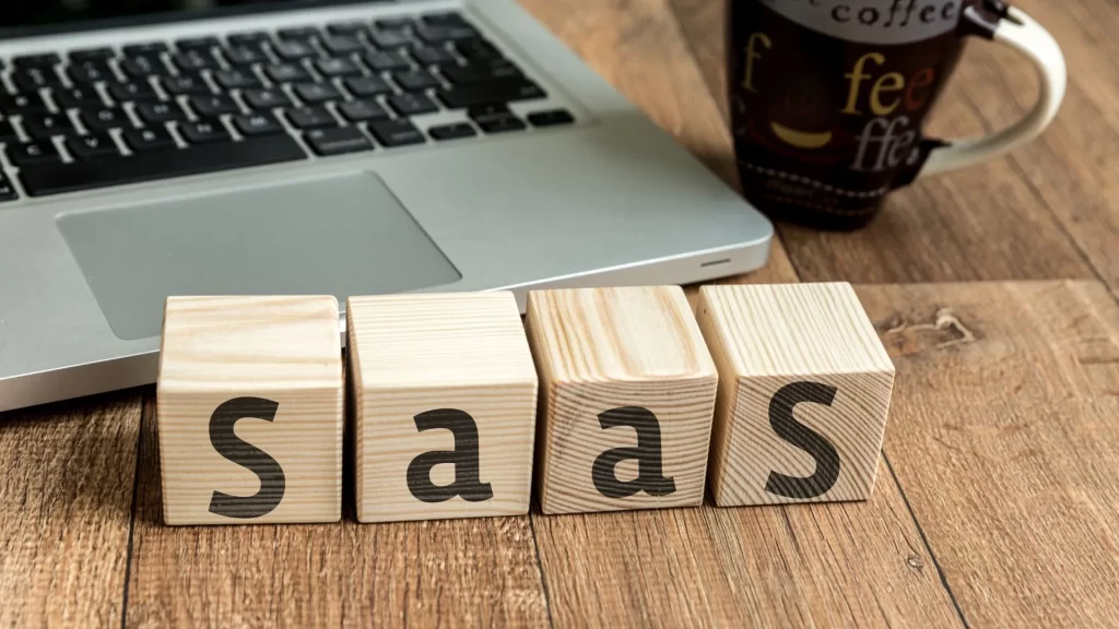 A laptop, a coffee mug, and some wooden blocks can be seen on the table. The letters S,a,a, and S are painted individually on the blocks.