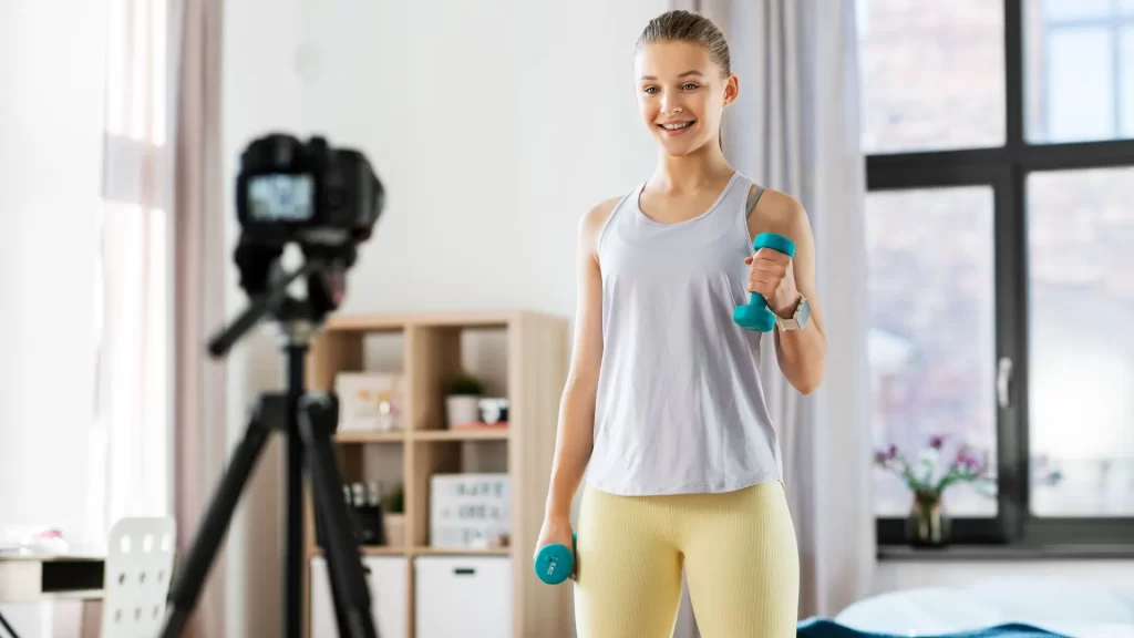 A young woman in workout gear is recording a workout video