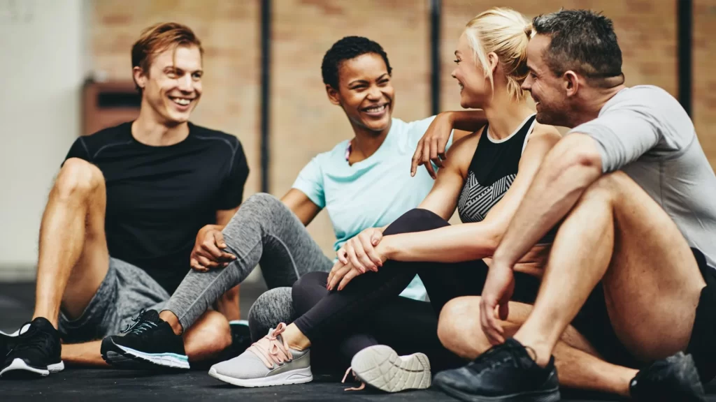 Four people sitting on a gym floor, talking and having fun