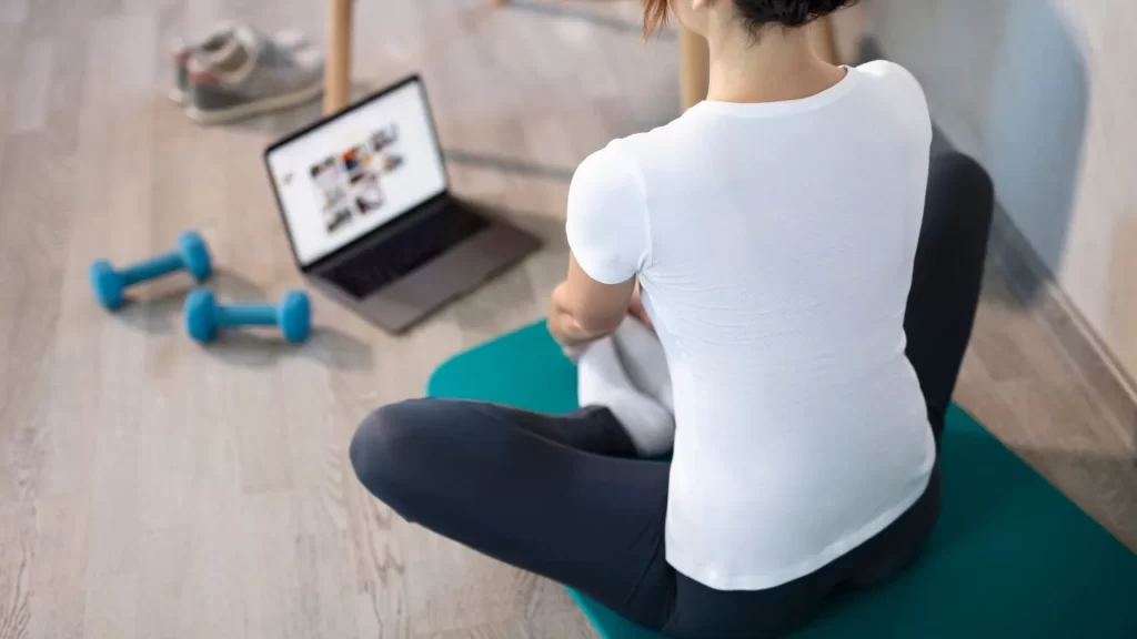 A personal trainer doing some stretches  with their laptop open 