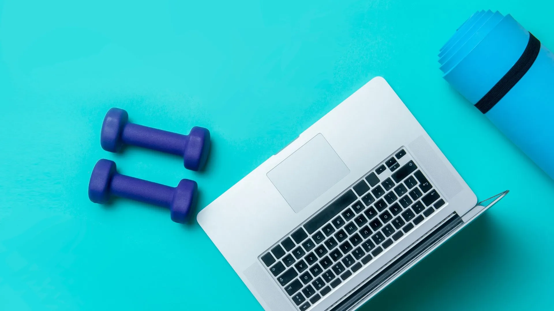 An open laptop and a pair of dumbbells laid out on a fitness mat