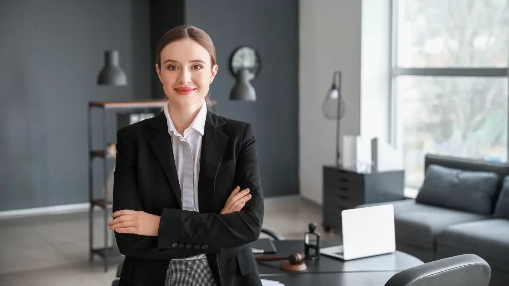 A female lawyer smiling at the camera while standing in her law firm with her arms crossed