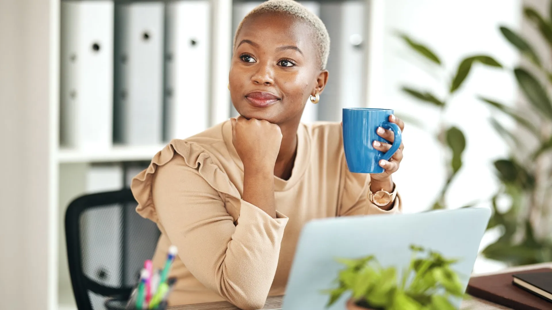 A woman with her laptop open and a cup of coffee in her hand is deep in thought