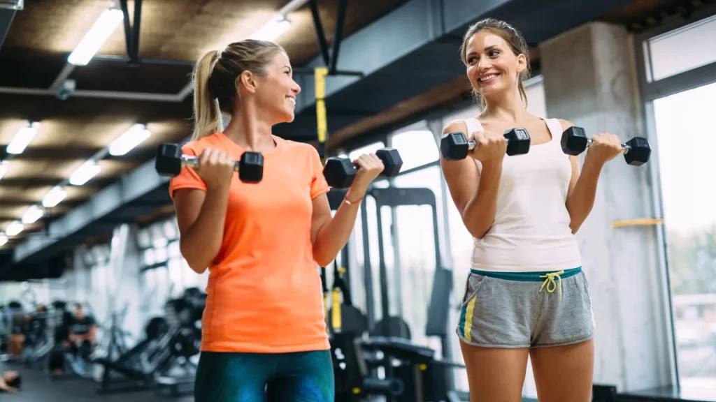 Two women lifting dumbbells inside a gym