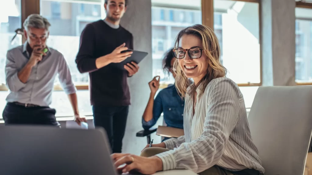 Four content marketing professionals are looking at a laptop screen. They have various expressions and seem to be in the middle of a brainstorming session.