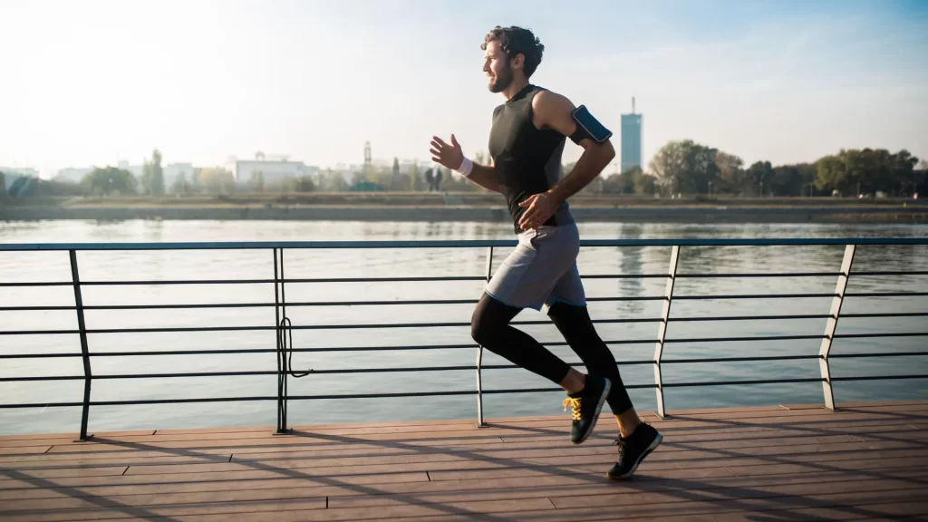 A male fitness enthusiast is jogging on the walkway beside a body of water