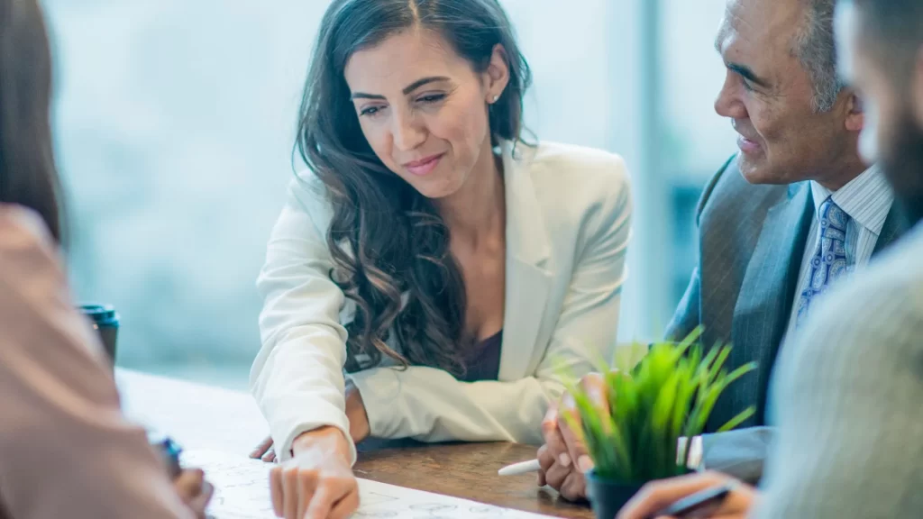 A woman who looks like she works for the marketing department is pointing something out in a piece of paper to her colleagues who seem to be lawyers.