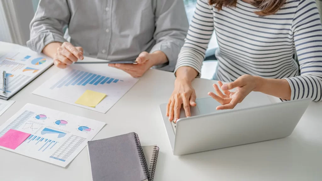 Two professionals talking about B2B Saas growth over a laptop and some printed out charts