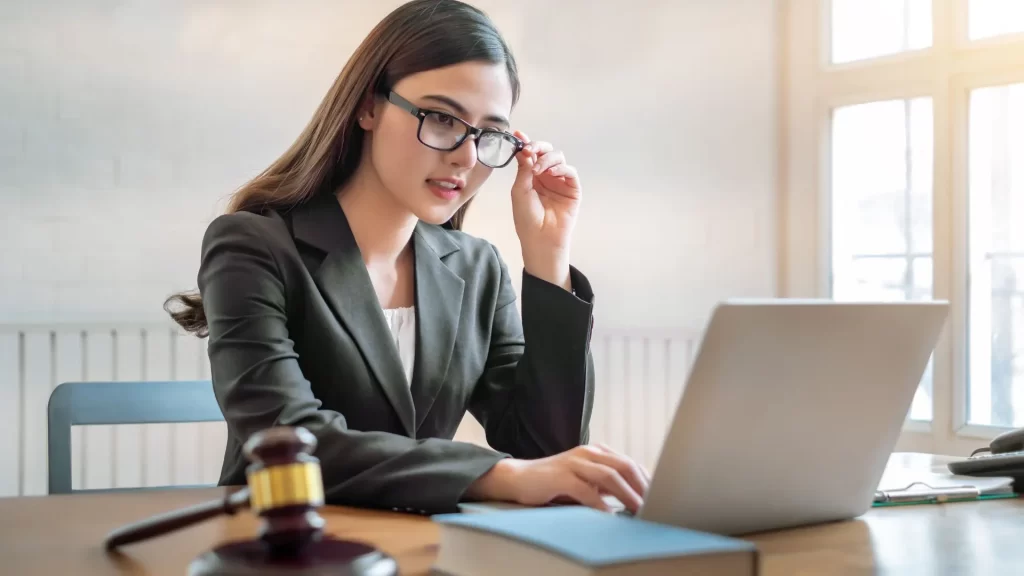 A female lawyer is adjusting her eyeglasses while looking intently at her laptop screen.